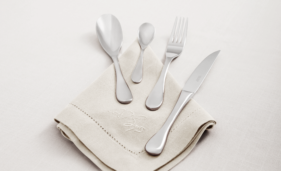 Elegant table setting with white ceramic dishes, polished silverware, glassware, and pink floral centerpieces on a green tablecloth.