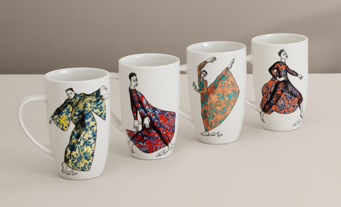 White ceramic mugs with colorful dancing girl designs, accompanied by matching plates in the background.