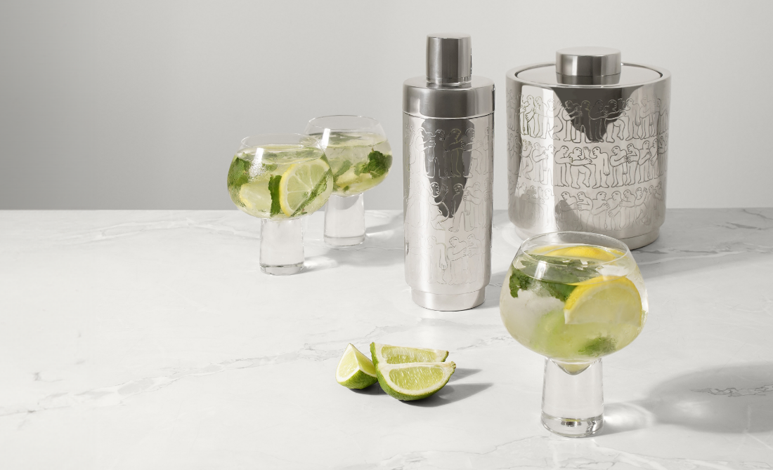 Collection of black bottles and containers with white artistic designs, including hand wash, lotion, hand sanitizer, and a candle, set against a neutral background.