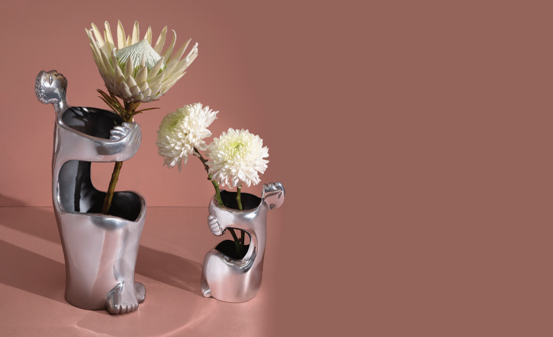 Polished metallic vases with a unique embrace design, holding white flowers, set against a neutral background.