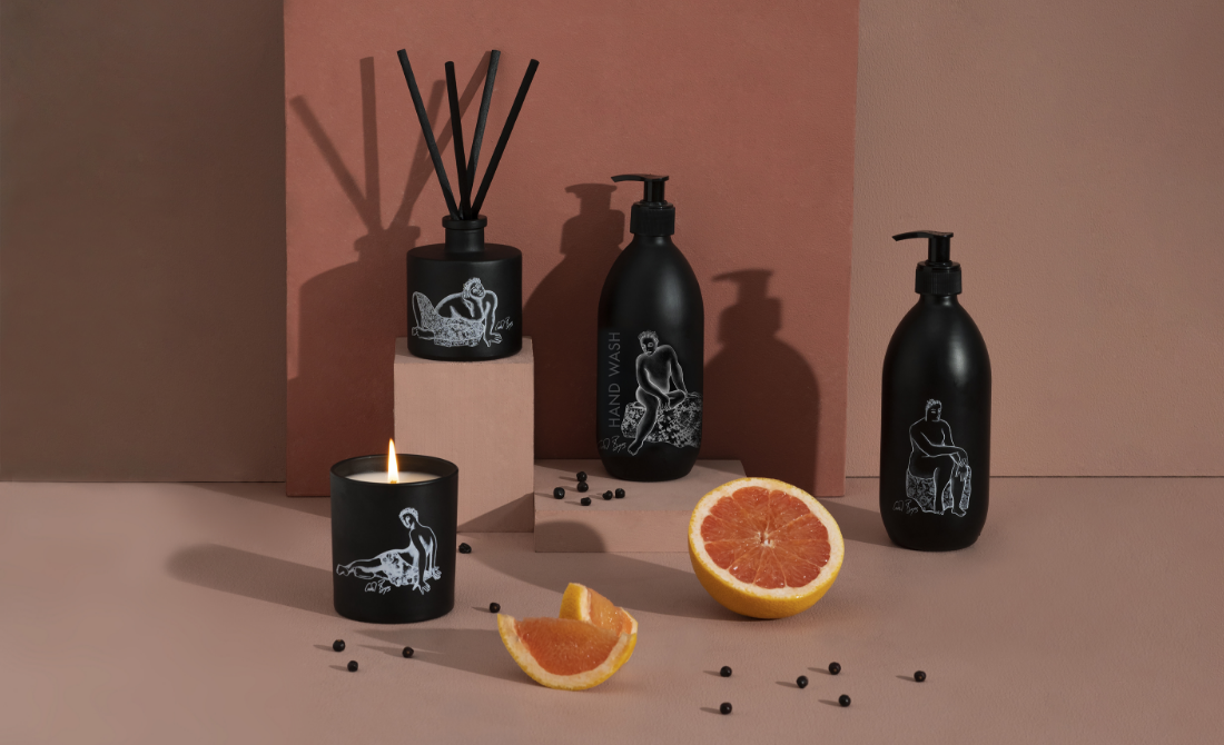 Collection of black bottles and containers with white artistic designs, including hand wash, lotion, hand sanitizer, and a candle, set against a neutral background.