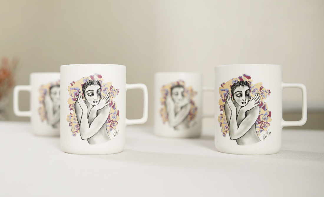 Three white ceramic mugs with colorful pop art designs of female figures, placed on a concrete surface with sugar cubes.