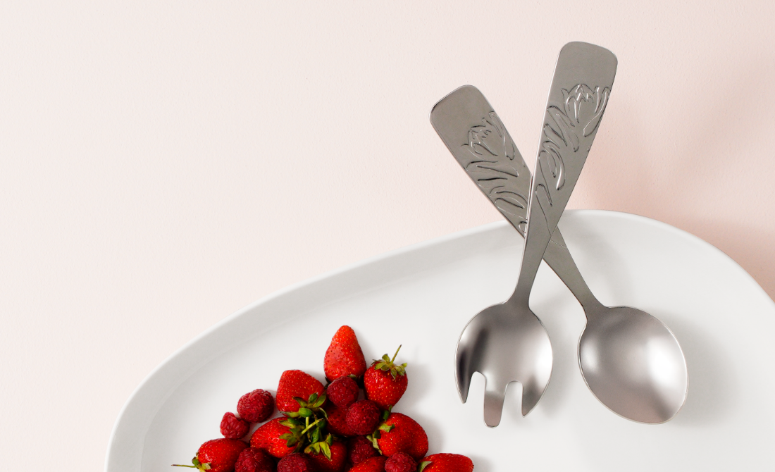 Polished spoon and spork with protea-themed handles, placed on a white plate.