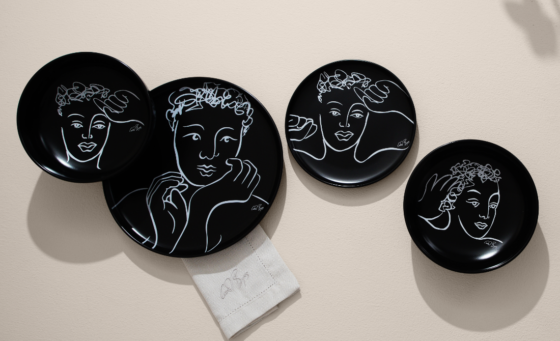 Artistic dinnerware set featuring white plates, bowls, and a mug with face sketches, arranged on a wooden table.