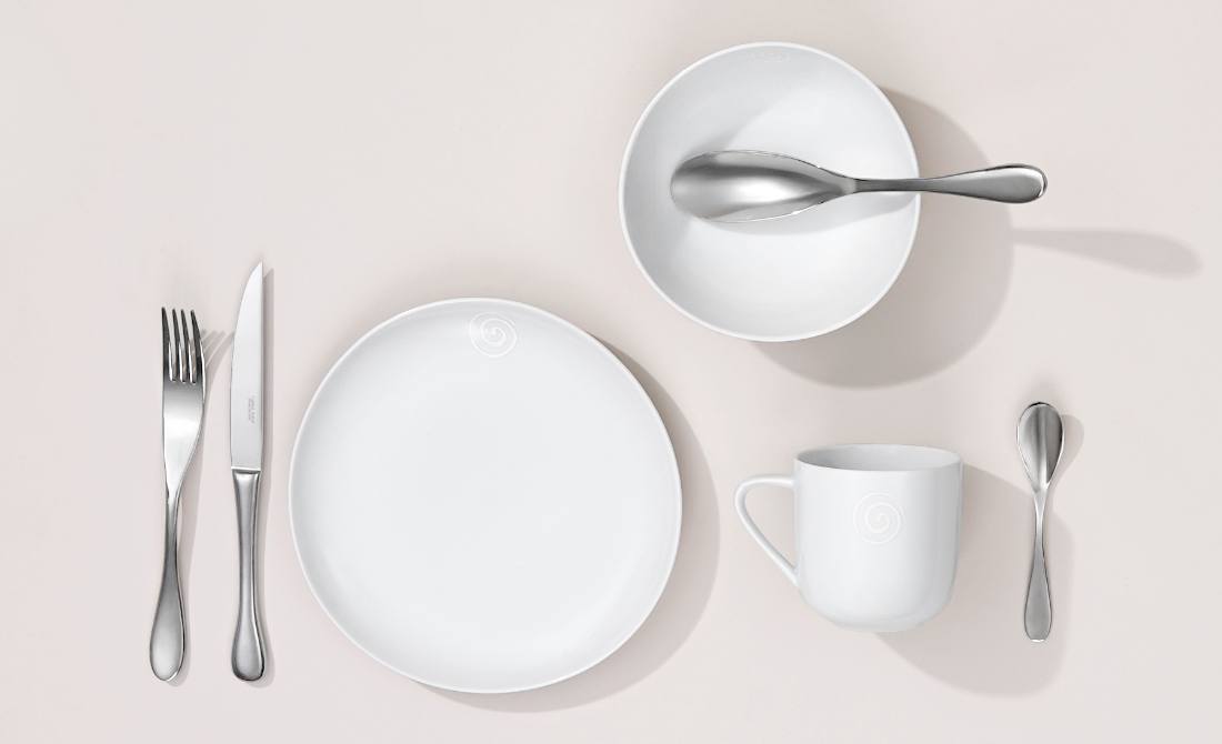 Polished metallic vase with a twisted design holding orange flowers, placed on a wooden table beside a leather sofa.