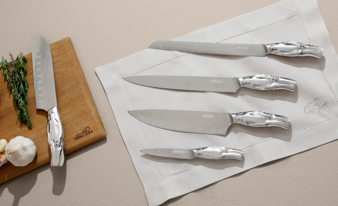 Polished metallic sculpture of a human figure mounted on a white wall, with a decorative vase of greenery nearby.
